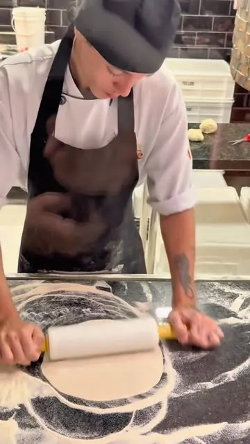 Pizzaiolo trabalhando a massa com rolo sobre mármore